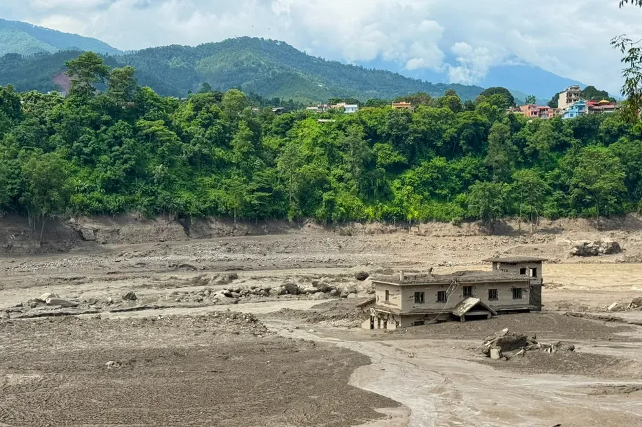 A damaged house stands precariously near the swollen, debris-choked banks of the Trishuli River after a flash floods in Nepal