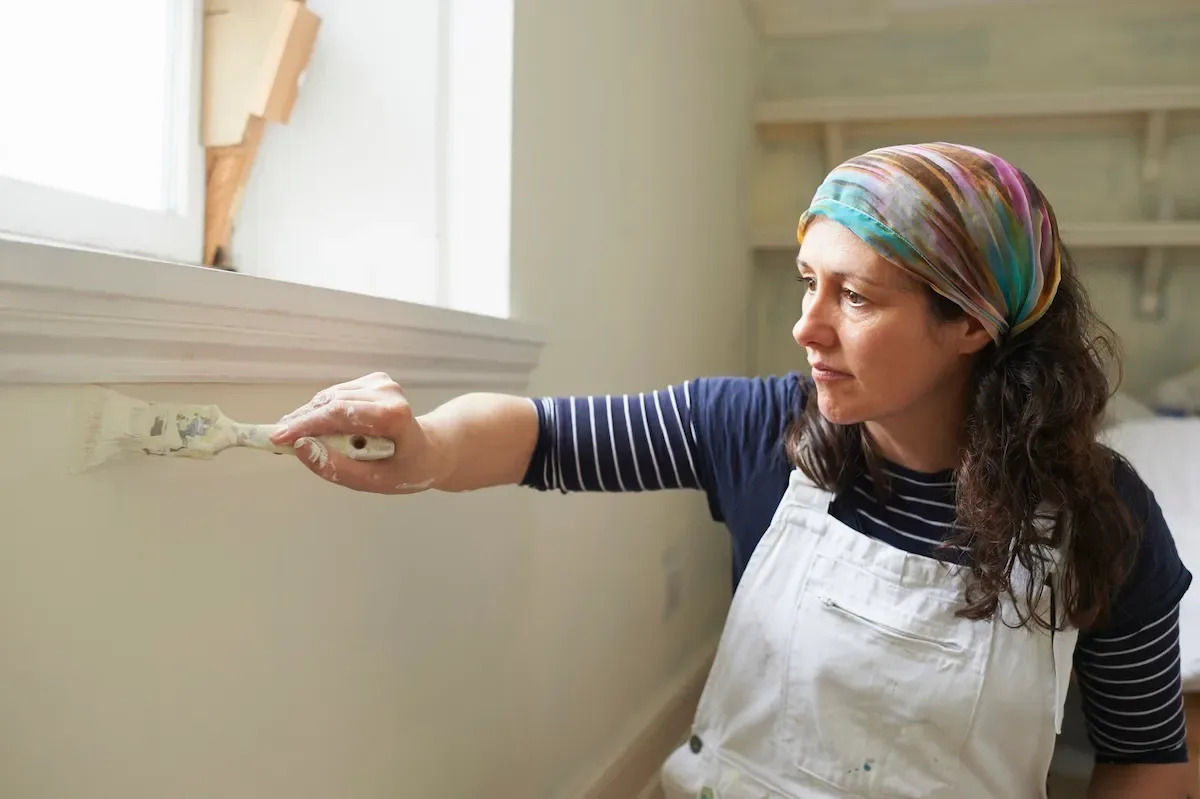 A person touching up paint on walls inside a home.