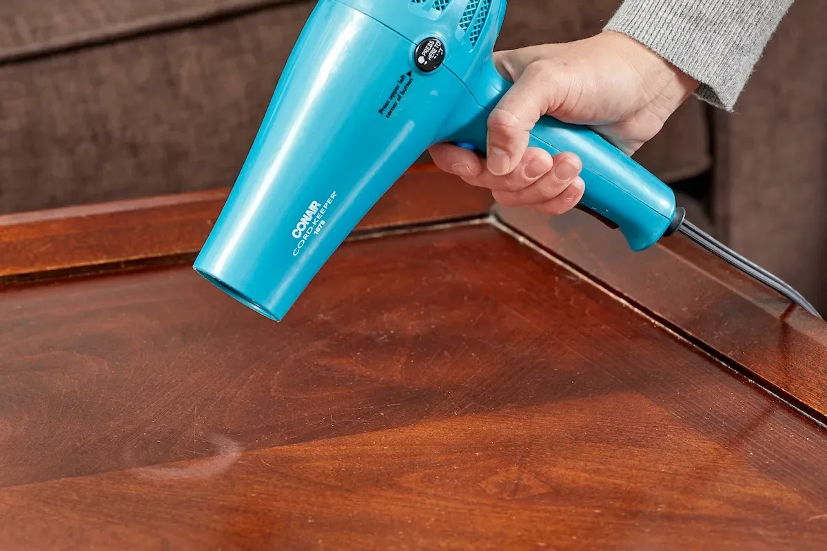 A person using a hair dryer to remove water stains from wood.