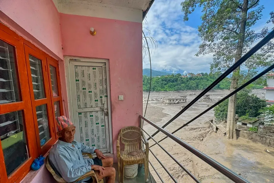 A resident sits on the balcony of his house surrounded by floodwaters and debris after flash floods caused the Trishuli