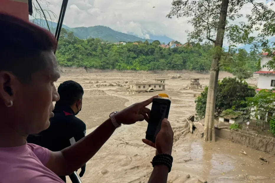 People take photographs and videos of the swollen, debris-choked banks of the Trishuli River after a flash floods in Nepal